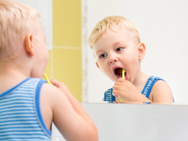 bambino si guarda allo specchio mentre si pulisce i denti