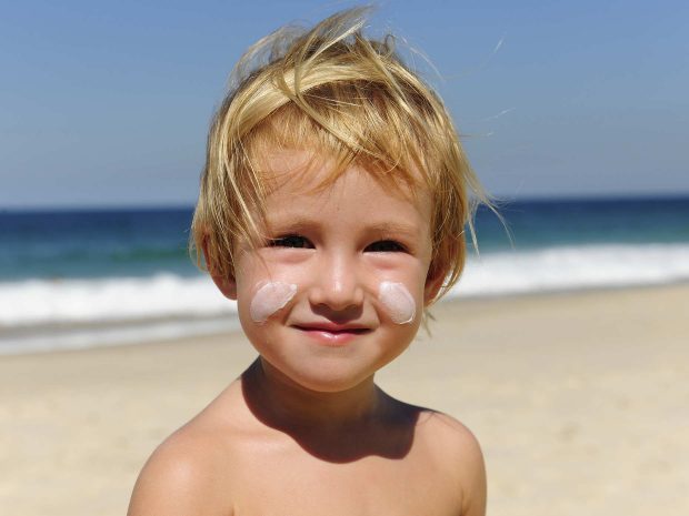 primo piano di un bambino biondo al mare con strisce di crema solare sulle guance